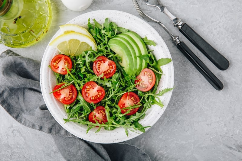 Green salad with leaves of arugula, tomatoes and avocado.