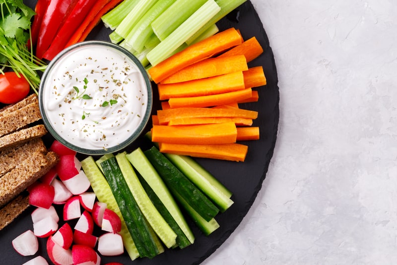 Healthy vegetables snack with yoghurt sauce on a slate stone round board.