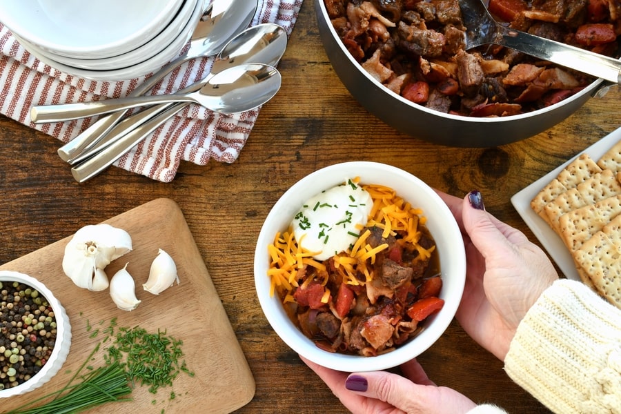 Woman setting down a bowl of beef & bacon keto chili.