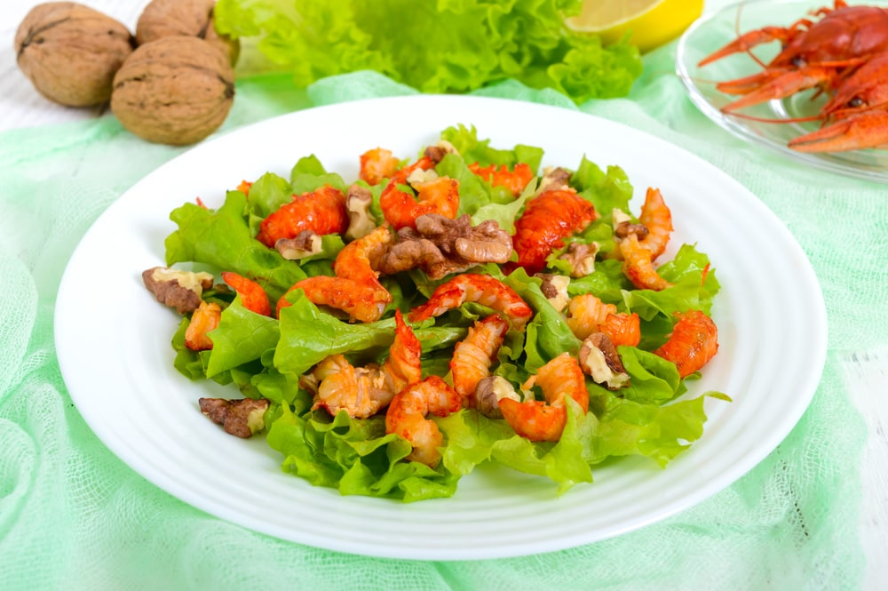 Light dietary spicy salad of lettuce and seafood on a white wooden background.